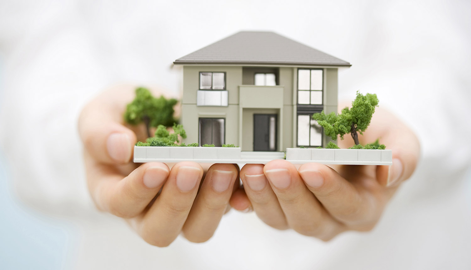 Hands holding miniature model of house.