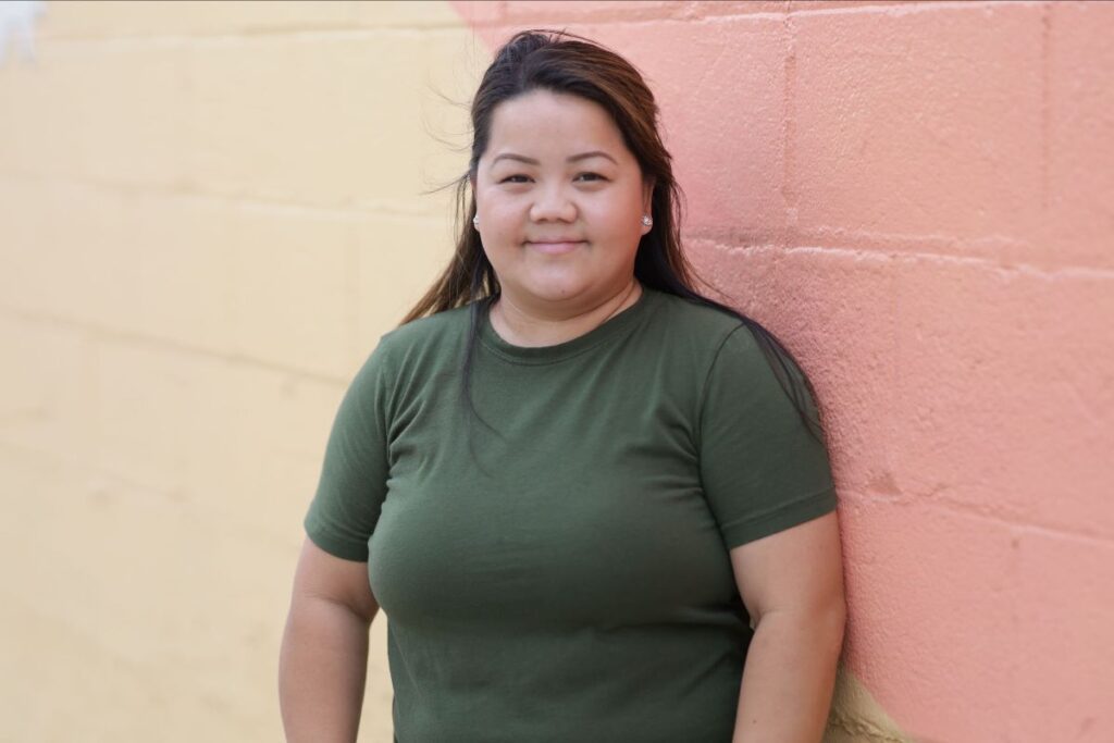 Image of a person standing against a painted wall, wearing a green t-shirt.